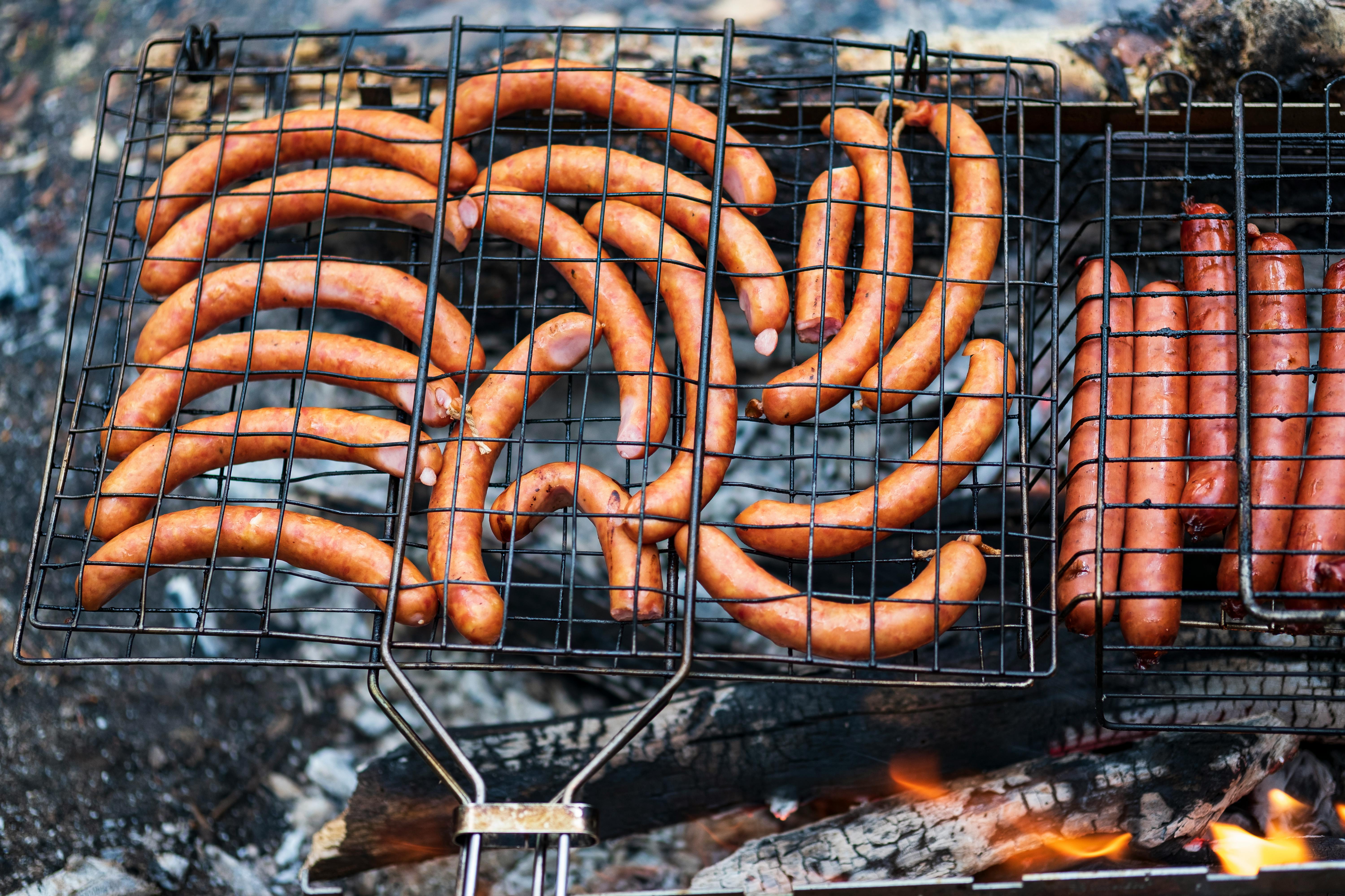 Delicious array of sausages grilling over charcoal flames, perfect for an outdoor picnic.
