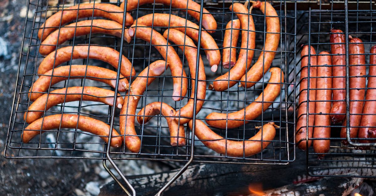 Delicious array of sausages grilling over charcoal flames, perfect for an outdoor picnic.