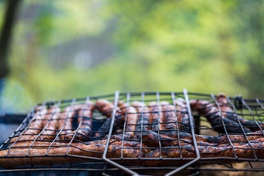 Grilled sausages sizzling on a barbecue outdoors with a blurred green background, perfect for summer cookouts.