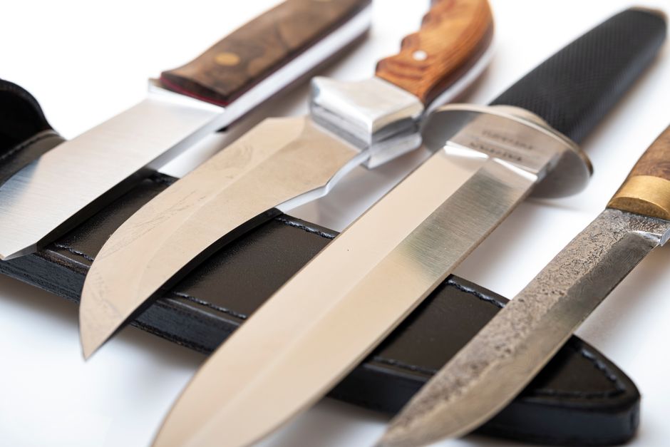 Close-up of different knives with diverse handles and blades on a black leather sheath.