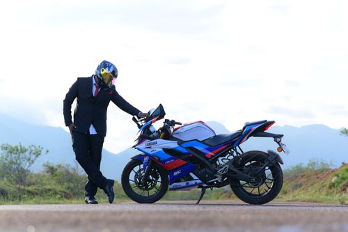 Free A man in a suit and helmet leans on a Yamaha motorcycle on a scenic road. Stock Photo
