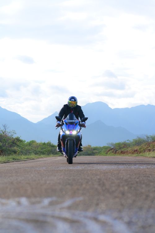 Free Motorcyclist riding Yamaha on rural road with mountain backdrop, capturing the thrill of adventure. Stock Photo