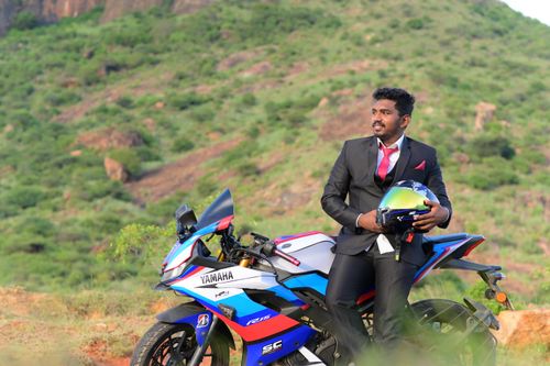 Free Man in a formal suit holding a helmet sits on a Yamaha motorcycle in a scenic rural area. Stock Photo