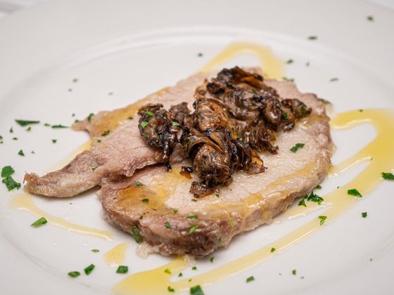 Slice of roast pork loin topped with dark sauteed mushrooms, parsley and olive oil