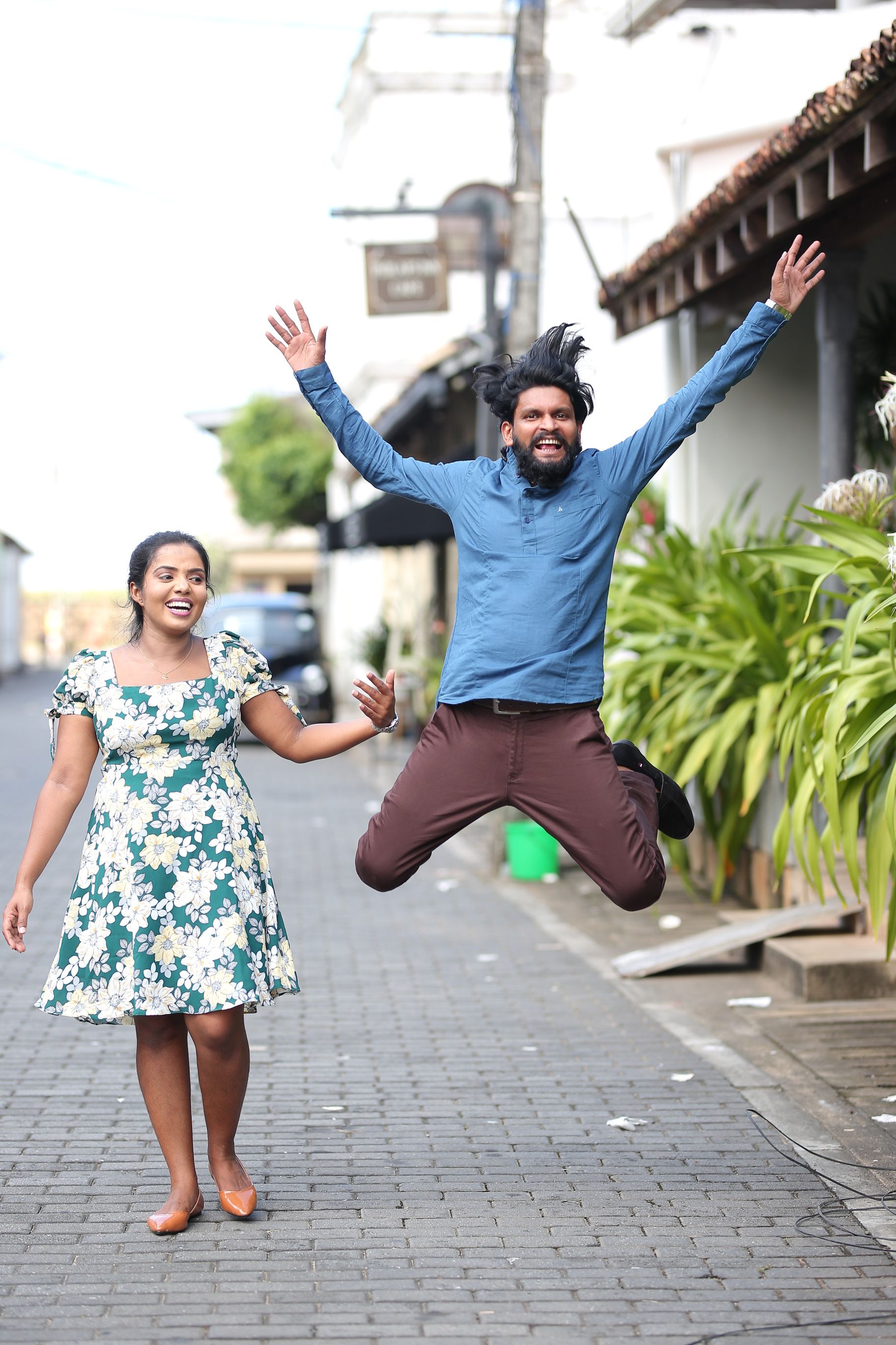 A happy couple laughing and jumping on a vibrant city street, showcasing urban joy and love.