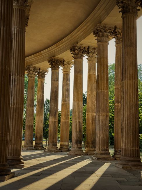 Sunlit colonnade with classic columns creating dramatic shadows and a vintage feel.