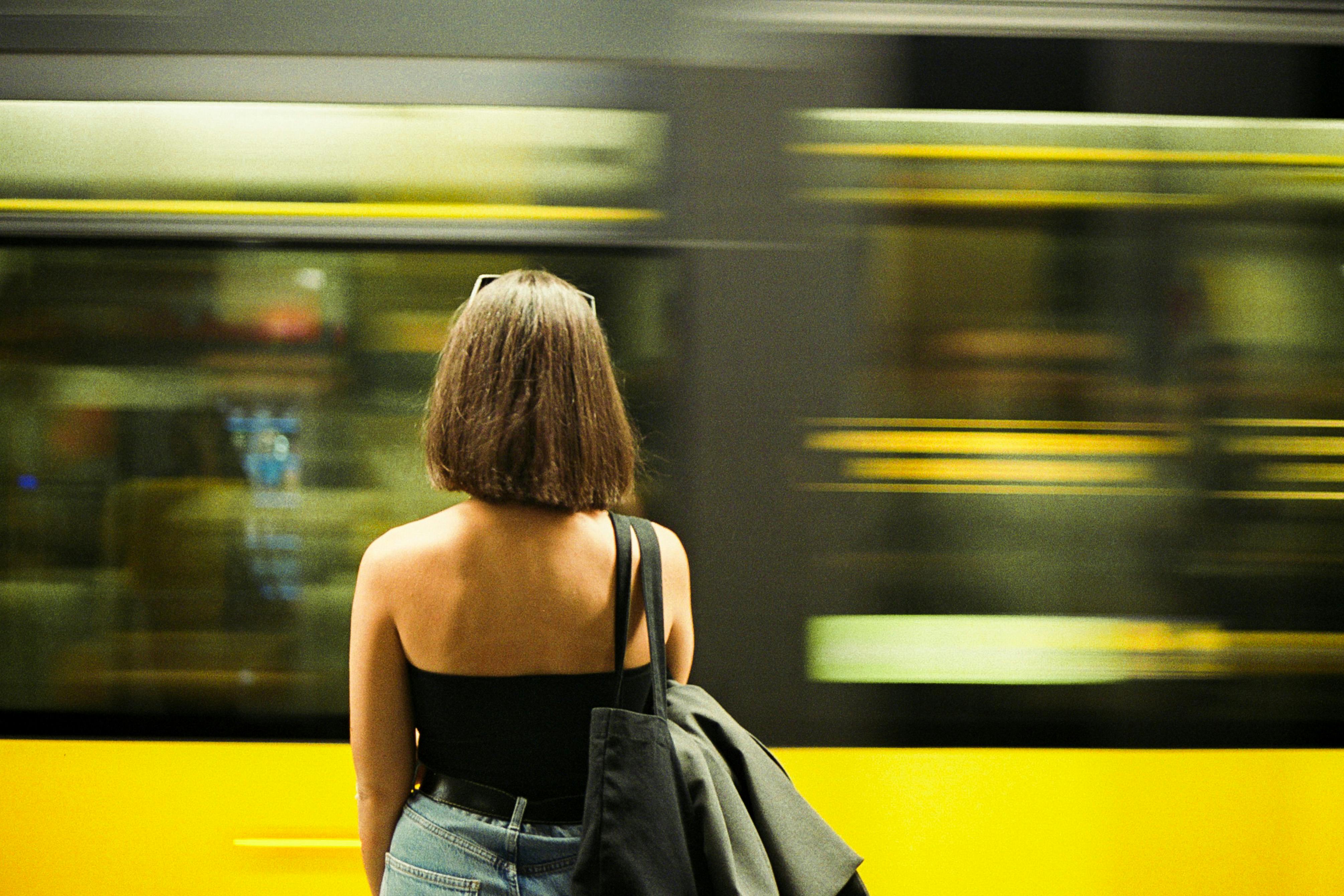 Rear view of a woman at a bustling metro station in Porto, Portugal, with a train speeding by.