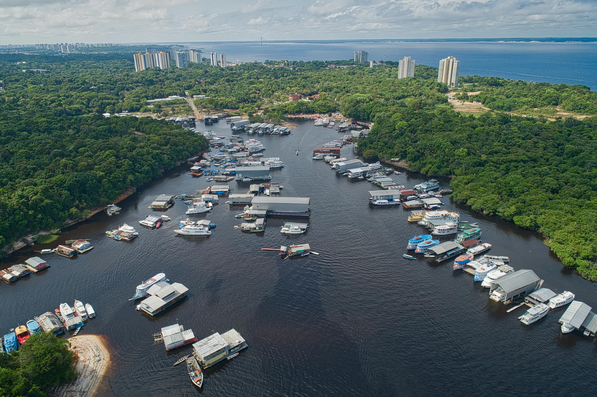 Discover Manaus's vibrant waterfront with floating houses and boats against dense Amazonian forest.