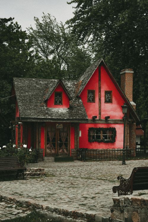 Free A picturesque red house with cobblestones, surrounded by lush greenery in a historic village setting. Stock Photo