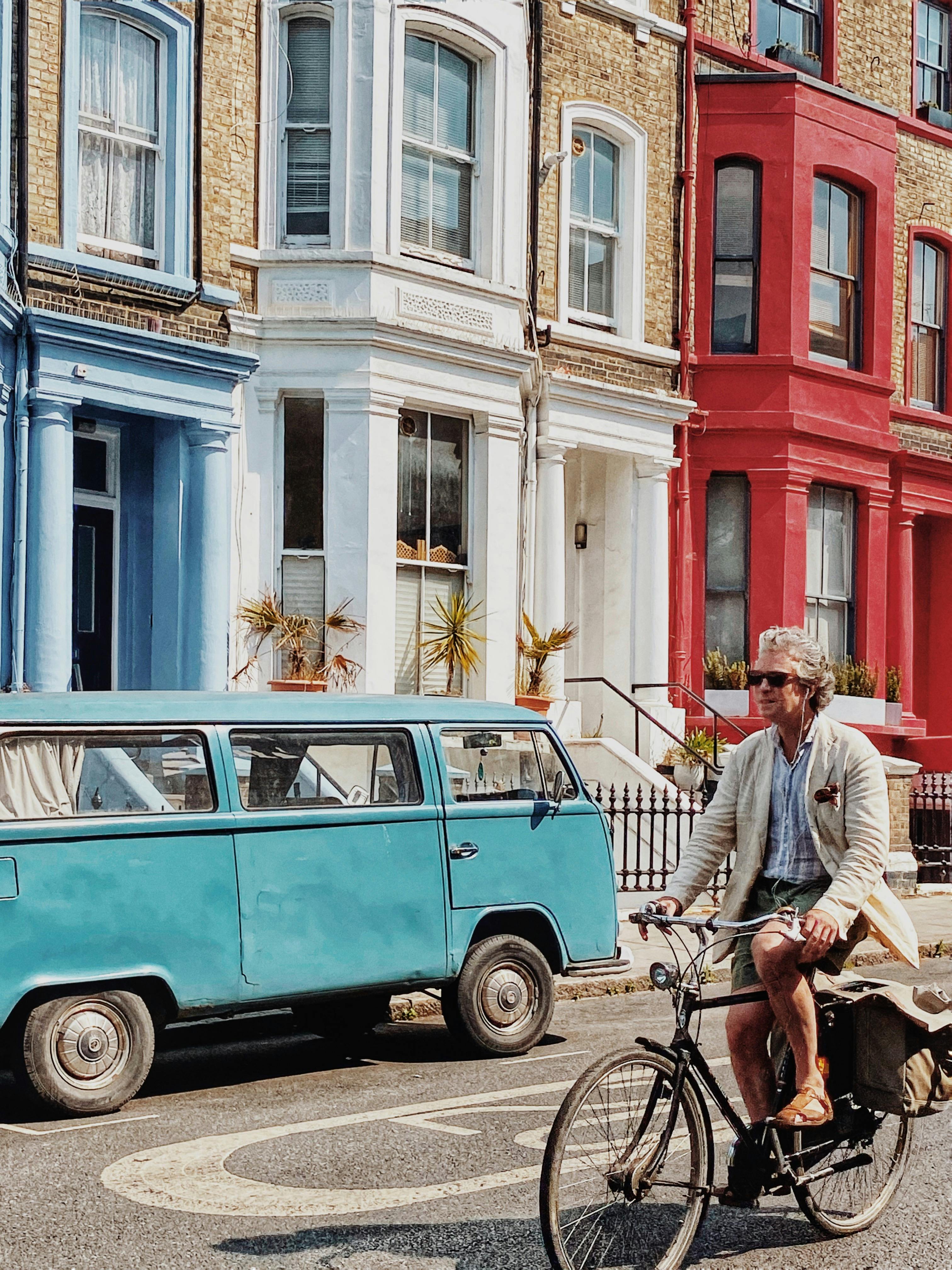 Free Man cycling past colorful London townhouses on a sunny day, embodying urban lifestyle. Stock Photo