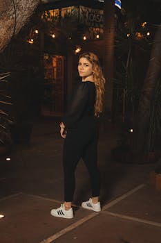 A young woman in a black outfit striking a pose on an urban pavement at night.