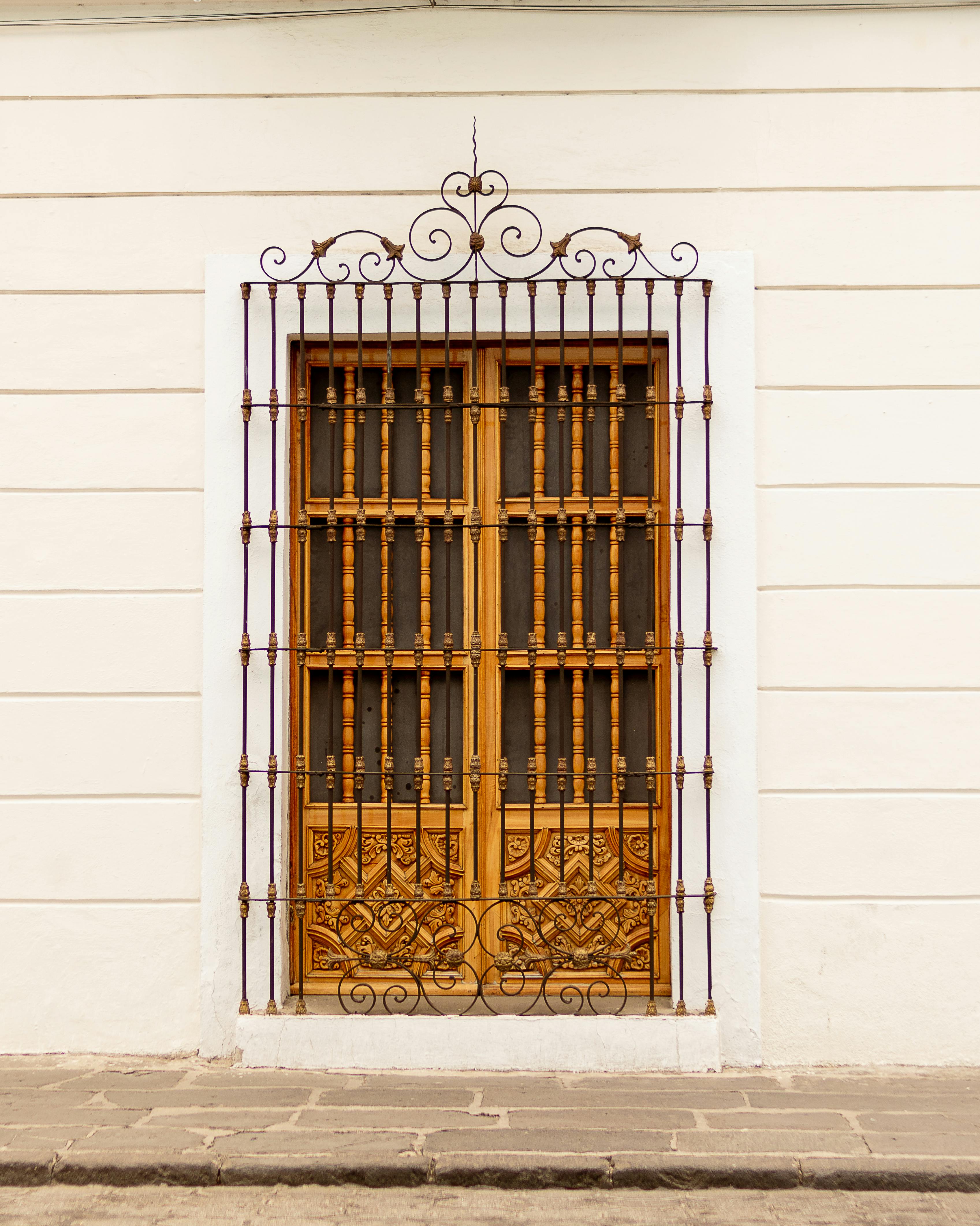 Ornate wooden door with intricate iron grill on a white wall, highlighting classic architecture.