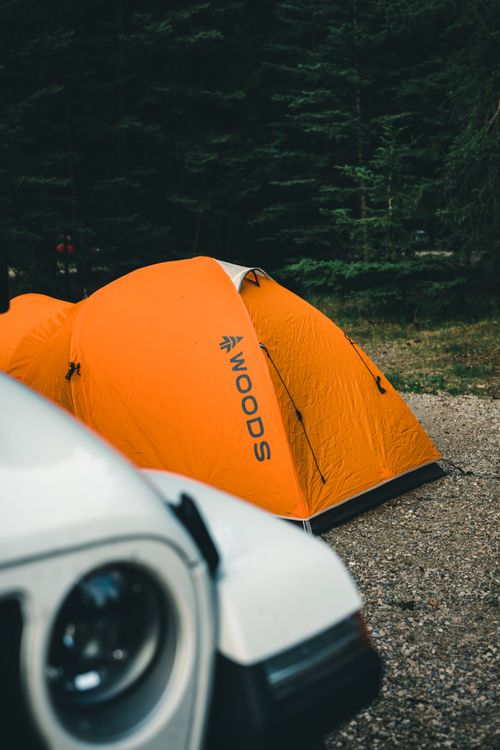 Free Camping scene in Jasper's forest with an orange tent and car under lush trees. Stock Photo
