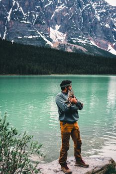 A man embraces a cat by the turquoise waters of Jasper Lake, surrounded by mountains.