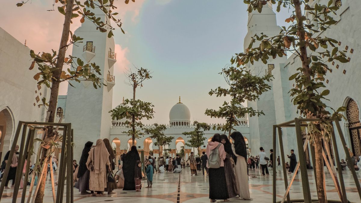 라마단 — A stunning view of the Sheikh Zayed Grand Mosque during sunset with people gathering under tree-lined pathways.