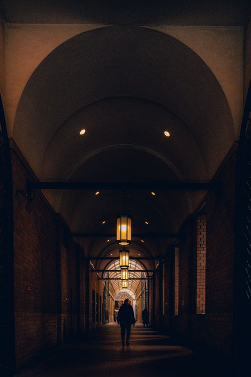 Free A silhouetted figure walks down a dimly lit corridor with arching ceilings and warm lighting. Stock Photo