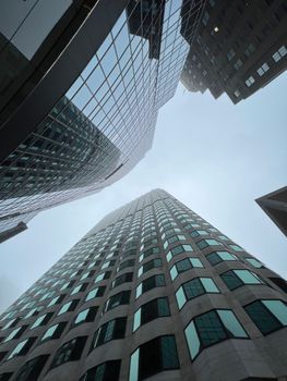 Modern glass skyscrapers reaching towards a cloudy sky in a bustling urban area.