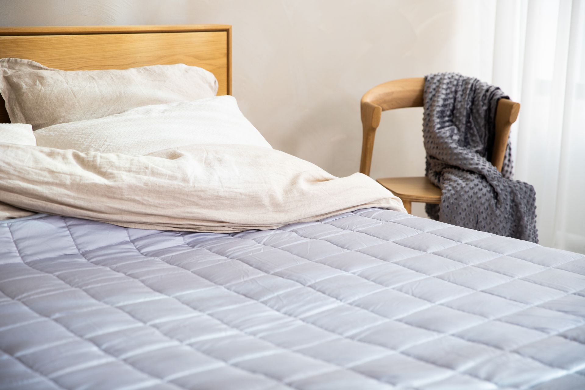 A cozy bedroom featuring a neatly made bed with pillows and a chair draped with a blanket.