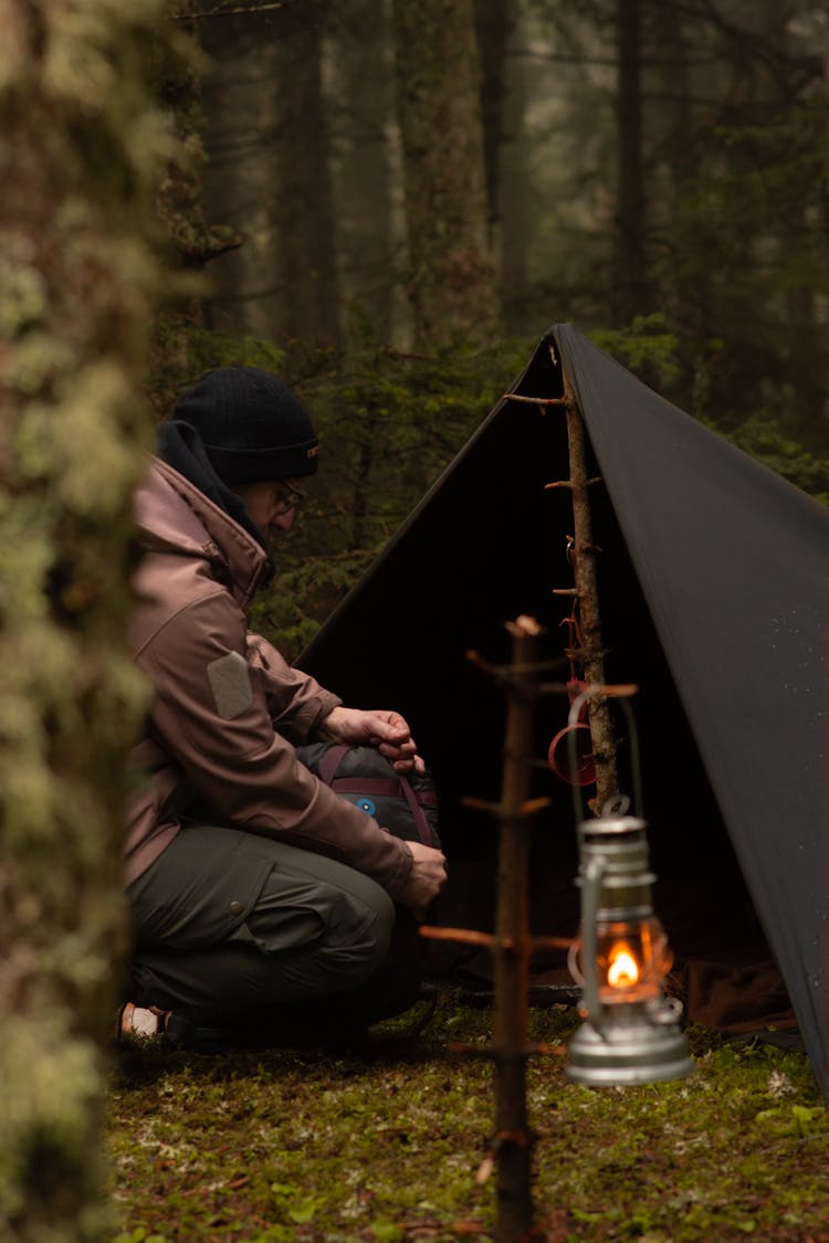 Man Sitting By A Black Camping Tent In A Forest