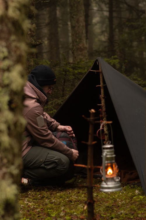 Free A man sits by a camping tent in a misty forest, illuminated by a kerosene lantern. Stock Photo