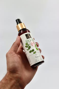 Close-up of a hand holding a rose glow toner bottle on a white background.