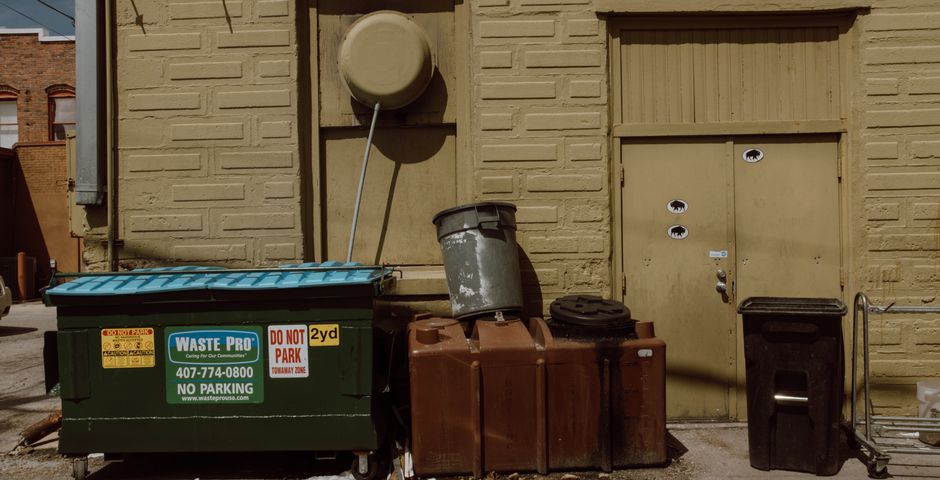 Waste bins and dumpsters in a service alleyway — the bin chamber at the base of the chute