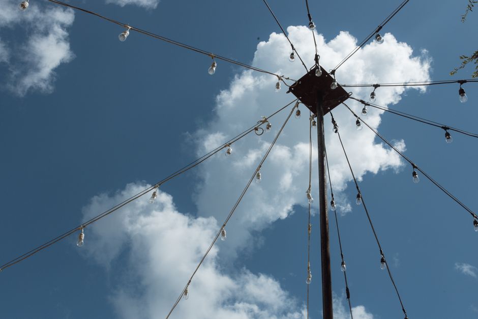 Low angle view of string lights on a post with fluffy clouds and a clear blue sky background.