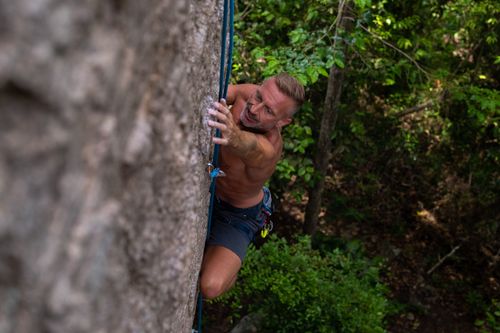 Free A man rock climbing a sheer cliff in a lush forest setting, showcasing strength and determination. Stock Photo