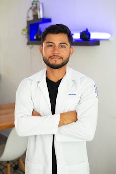 Portrait of a male doctor confidently posing with crossed arms, wearing a lab coat indoors.