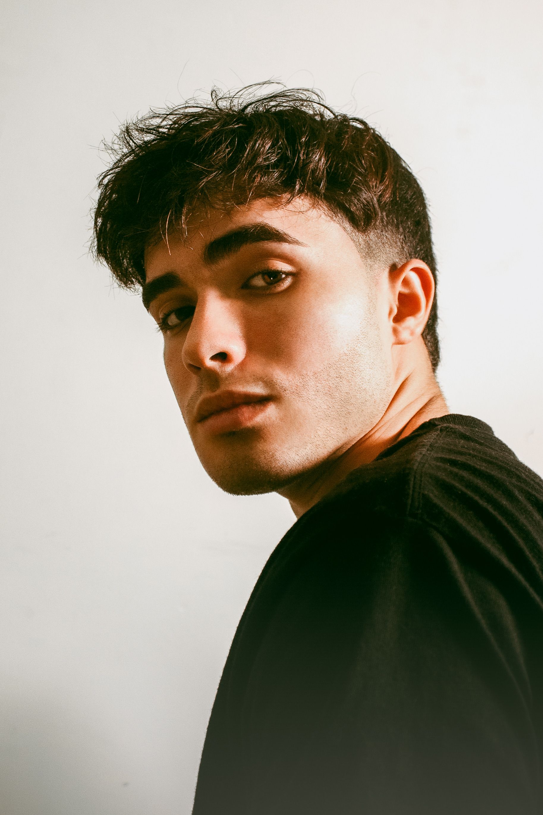 Close-up portrait of a young man with bushy eyebrows and bangs, wearing a black shirt.