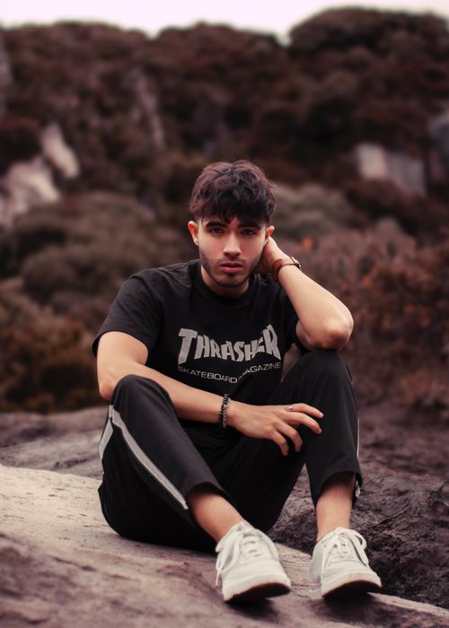 Free Young man in black clothing sitting on rock in natural setting, relaxed pose. Stock Photo