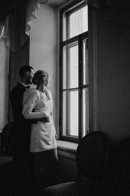 A stylish couple elegantly looking out a window in a classic black and white setting.