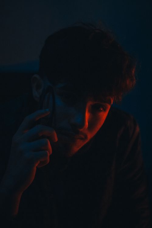 Free A man poses in dramatic red and blue lighting, creating a moody atmosphere. Stock Photo