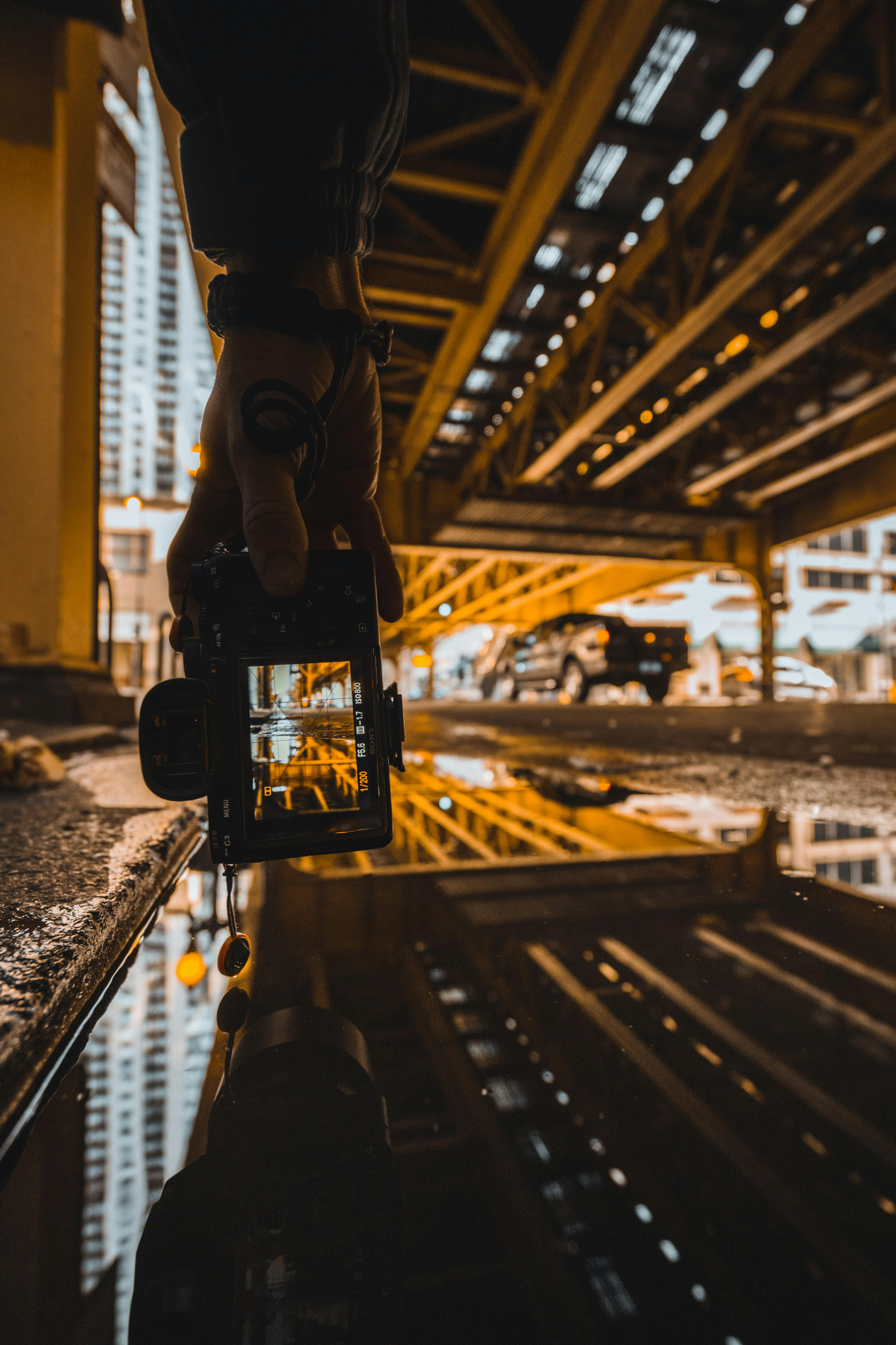 桥下水坑中，摄影师的手与城市景观形成了戏剧性的倒影