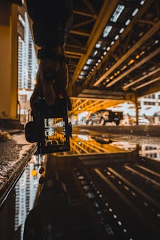 桥下水坑中，摄影师的手与城市景观形成了戏剧性的倒影