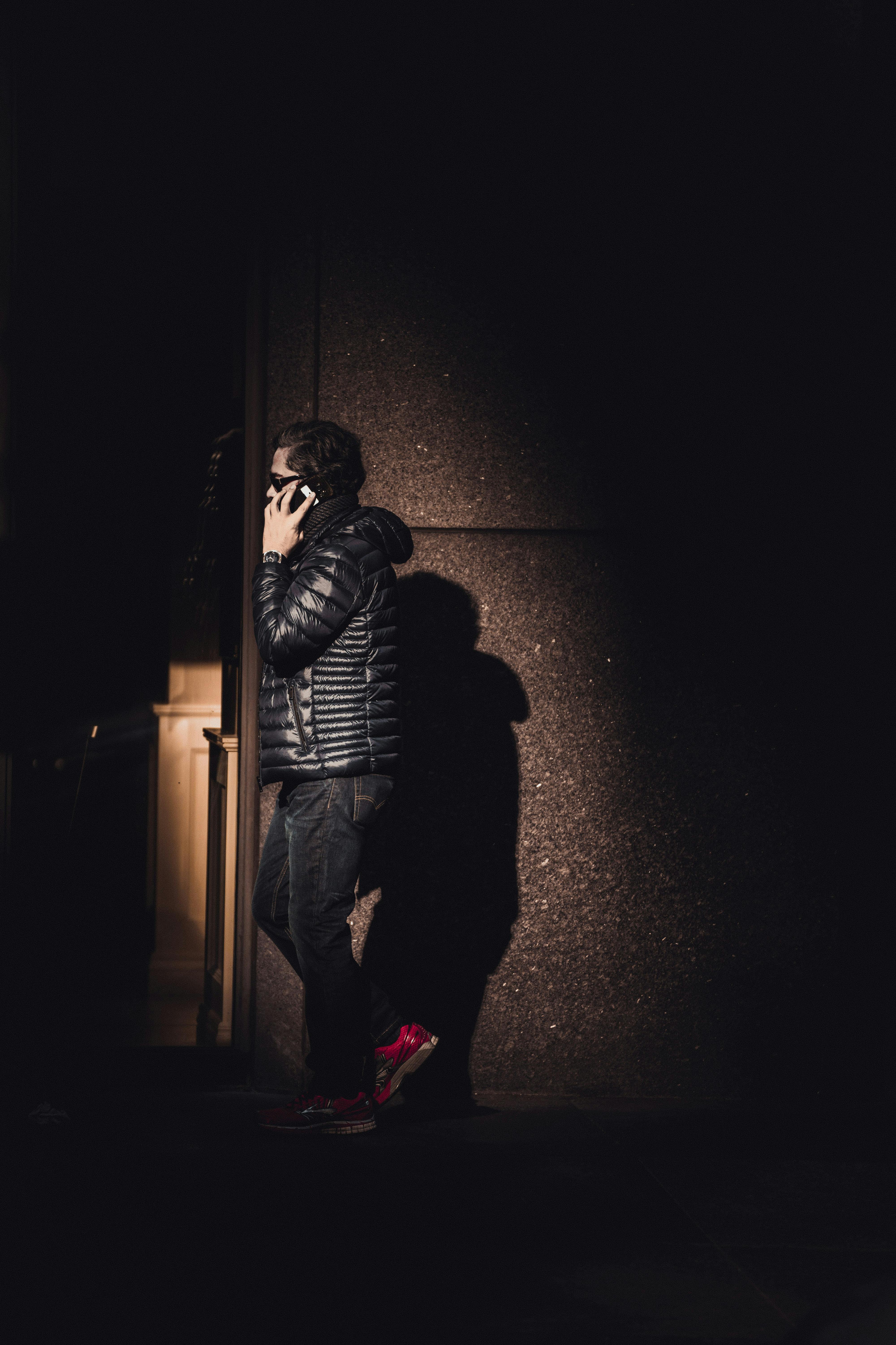 一名男子穿着羽绒服，在阴暗的城市小巷里打电话，凸显了夜间的城市生活