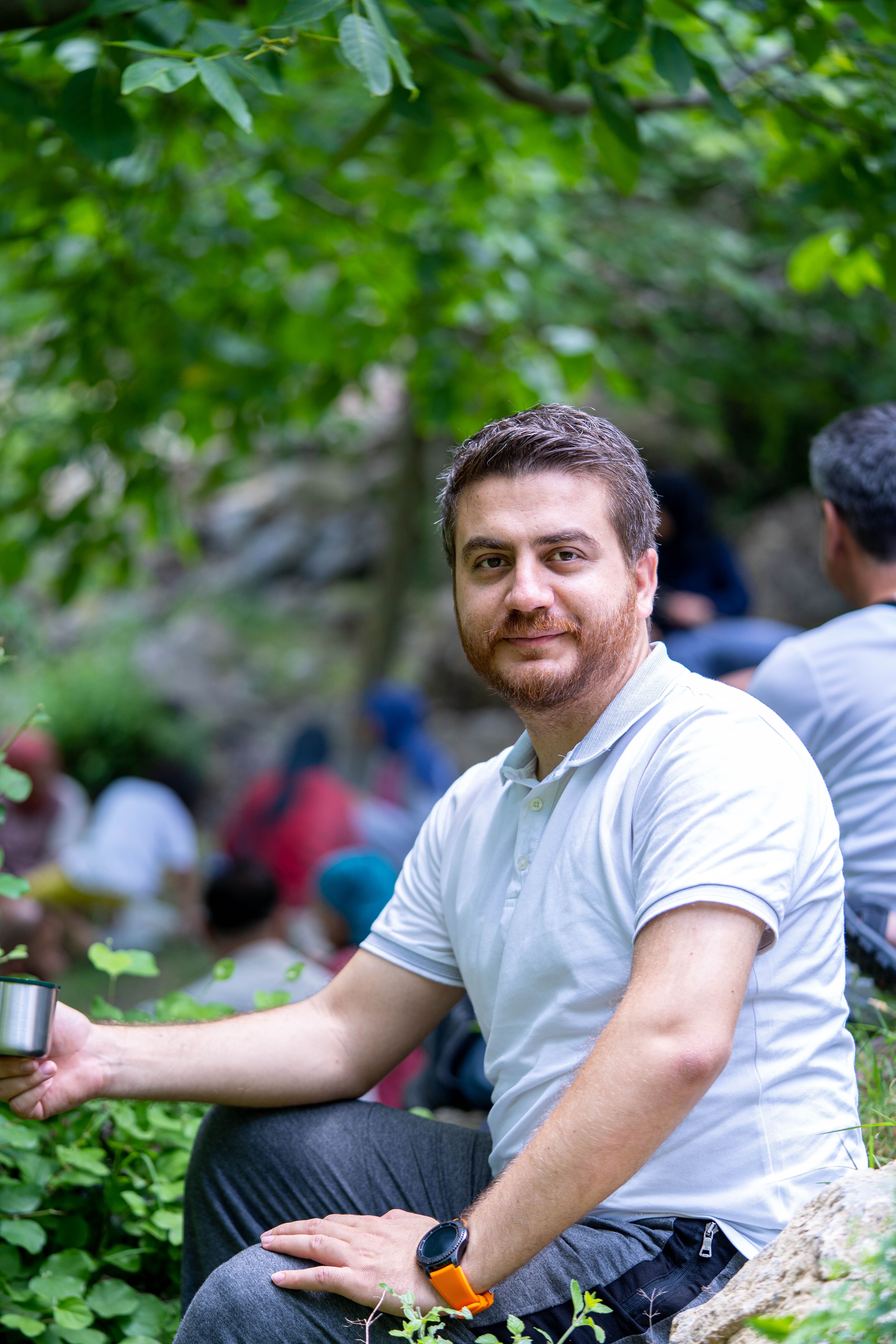 A man sitting outdoors in Kahramanmaraş, Türkiye, enjoying a scenic nature view with others in the background.