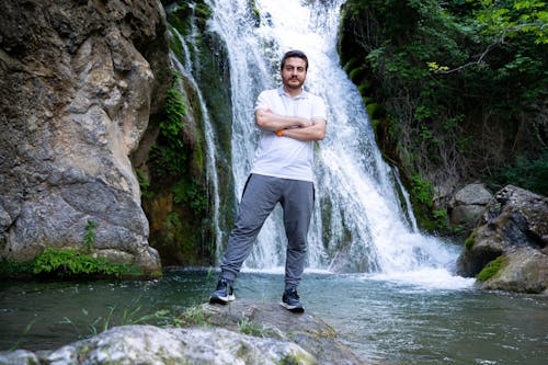 Man Standing with Arms Crossed by Waterfall