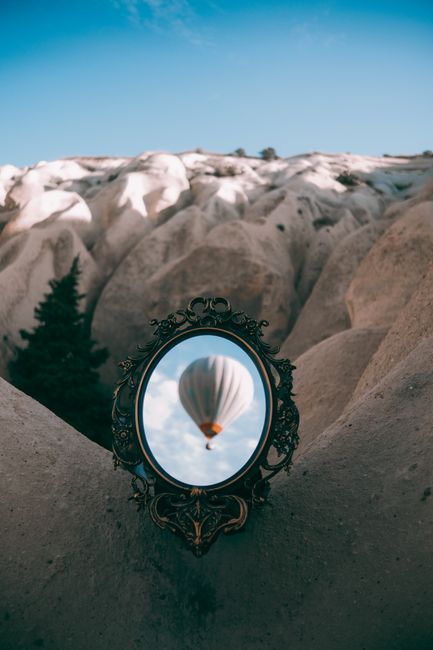 A hot air balloon reflected in a mirror amidst the unique rock formations of Cappadocia, Türkiye.