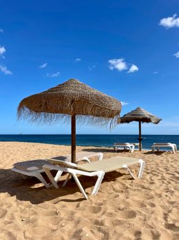 Tranquil beach scene with straw umbrellas and loungers under a clear blue sky.