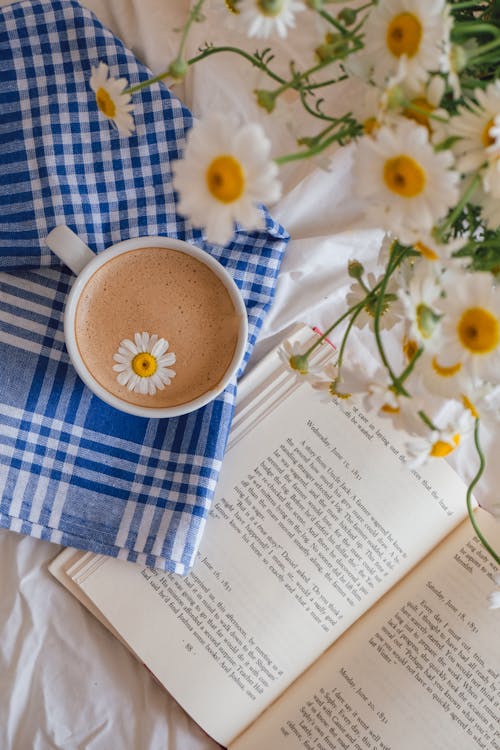 Cup of Coffee Next to Book and Bouquet of Chamomile