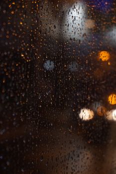 Close-up of raindrops on window glass with blurred city lights in a night backdrop.