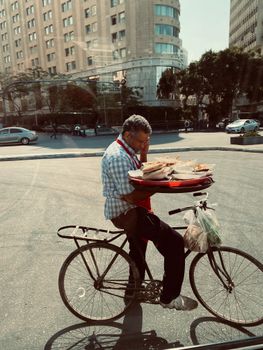 A man skillfully balances food trays on a bicycle in an urban Cairo street, showcasing daily life in the city.