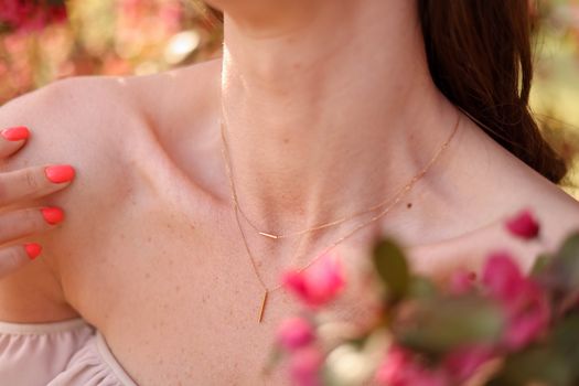 Close-up of a woman with a delicate necklace, showcasing beauty and elegance in a blooming summer garden.