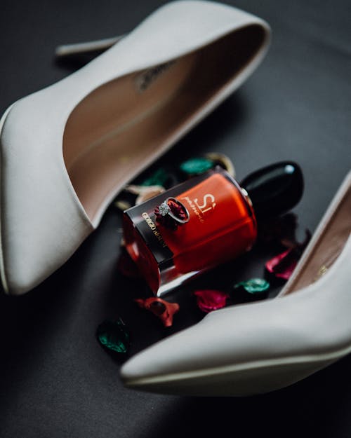 Close-up of a Bottle of Red Nail Polish and a Ring Lying between Heels 