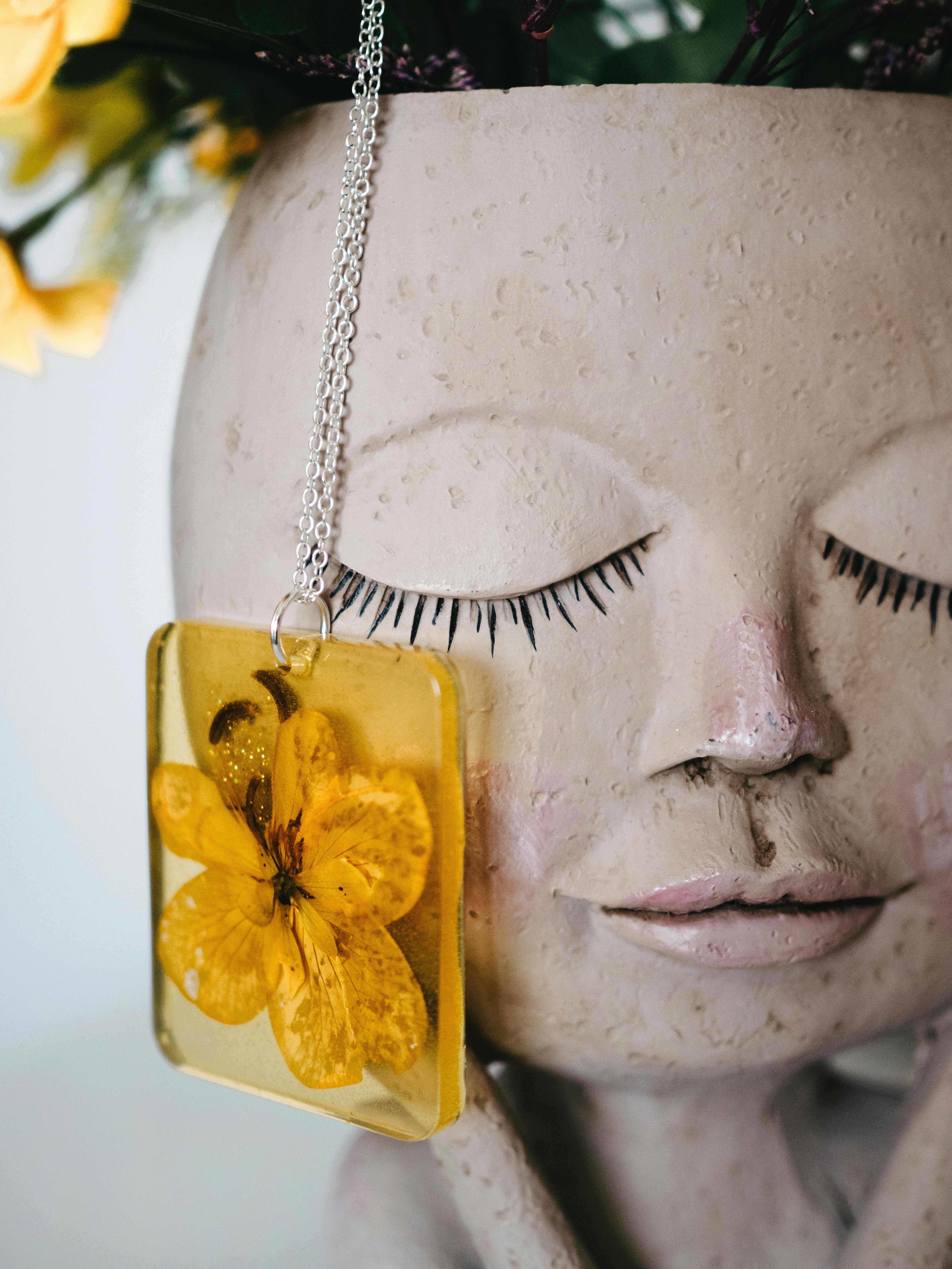Close-up of a handmade resin necklace with a yellow flower on a creative sculpture.