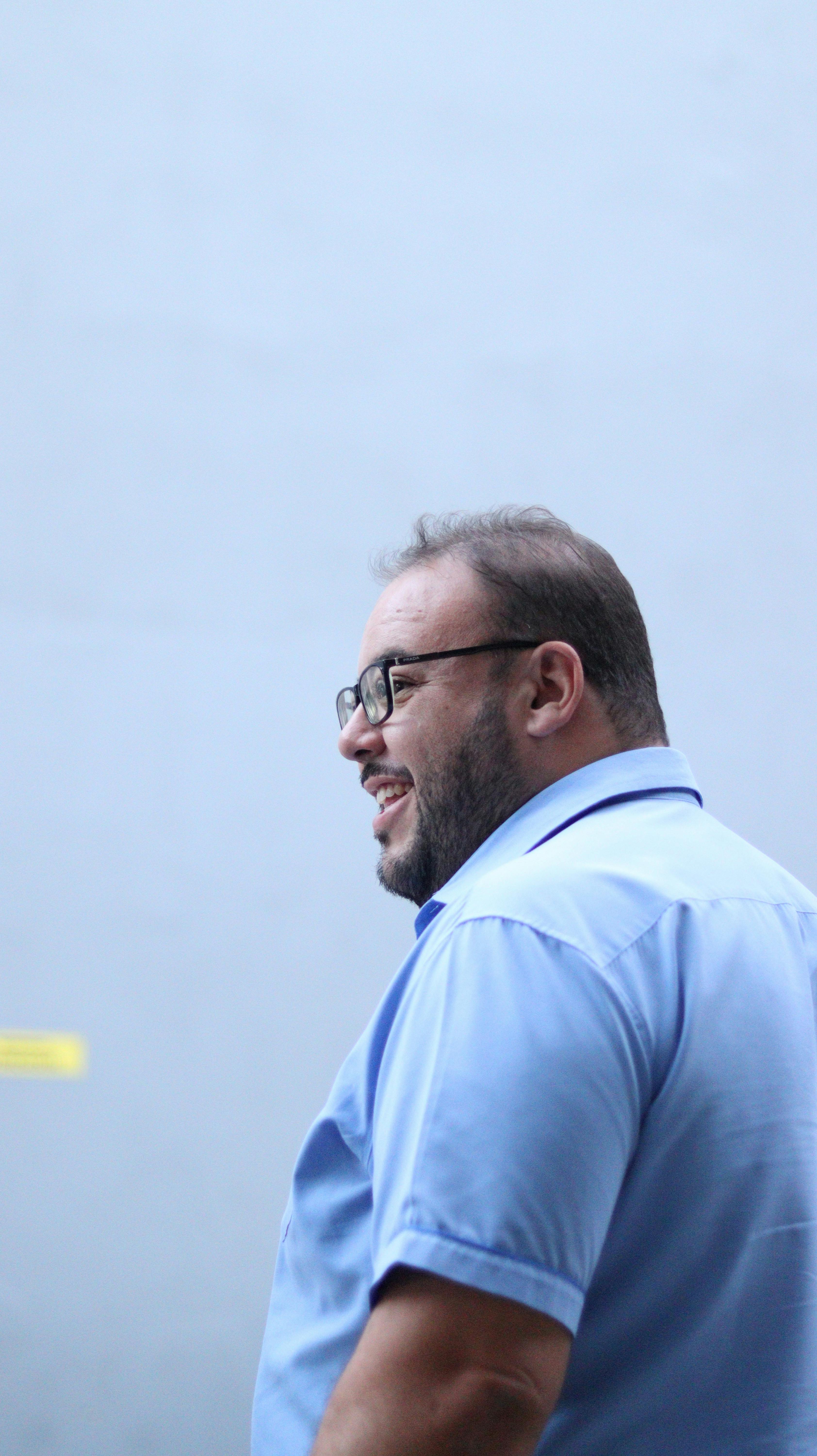 Cheerful man with glasses smiling against a blue background outdoors in Ibirité, Brazil.