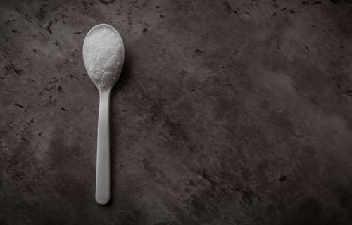Free A white spoon filled with sugar resting on a rustic dark background. Stock Photo
