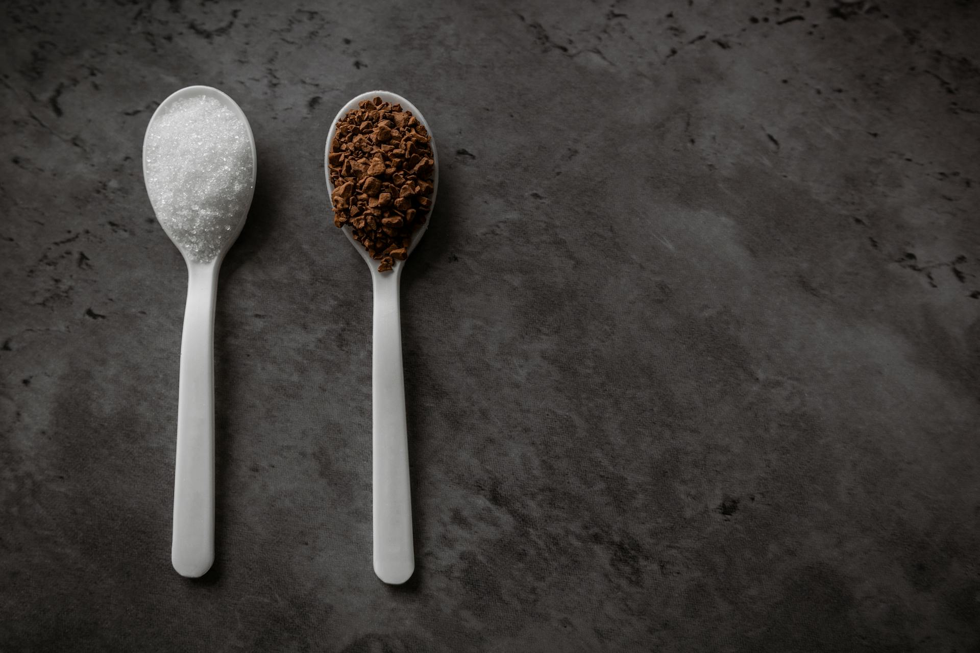 Two spoonfuls of instant coffee and sugar on the kitchen counter in equal portions. Top view flat lay with empty space for text. Excess sugar concept