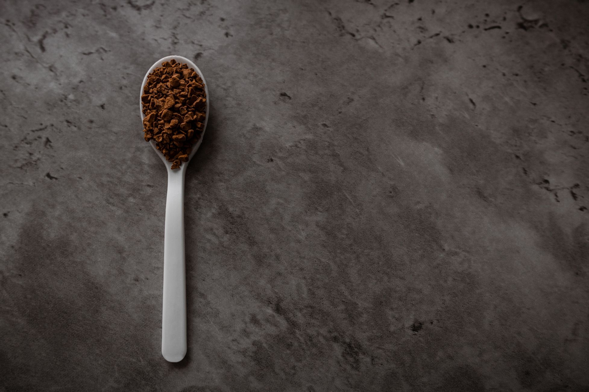A spoon filled with instant coffee on a dark textured background, perfect for beverage themes.